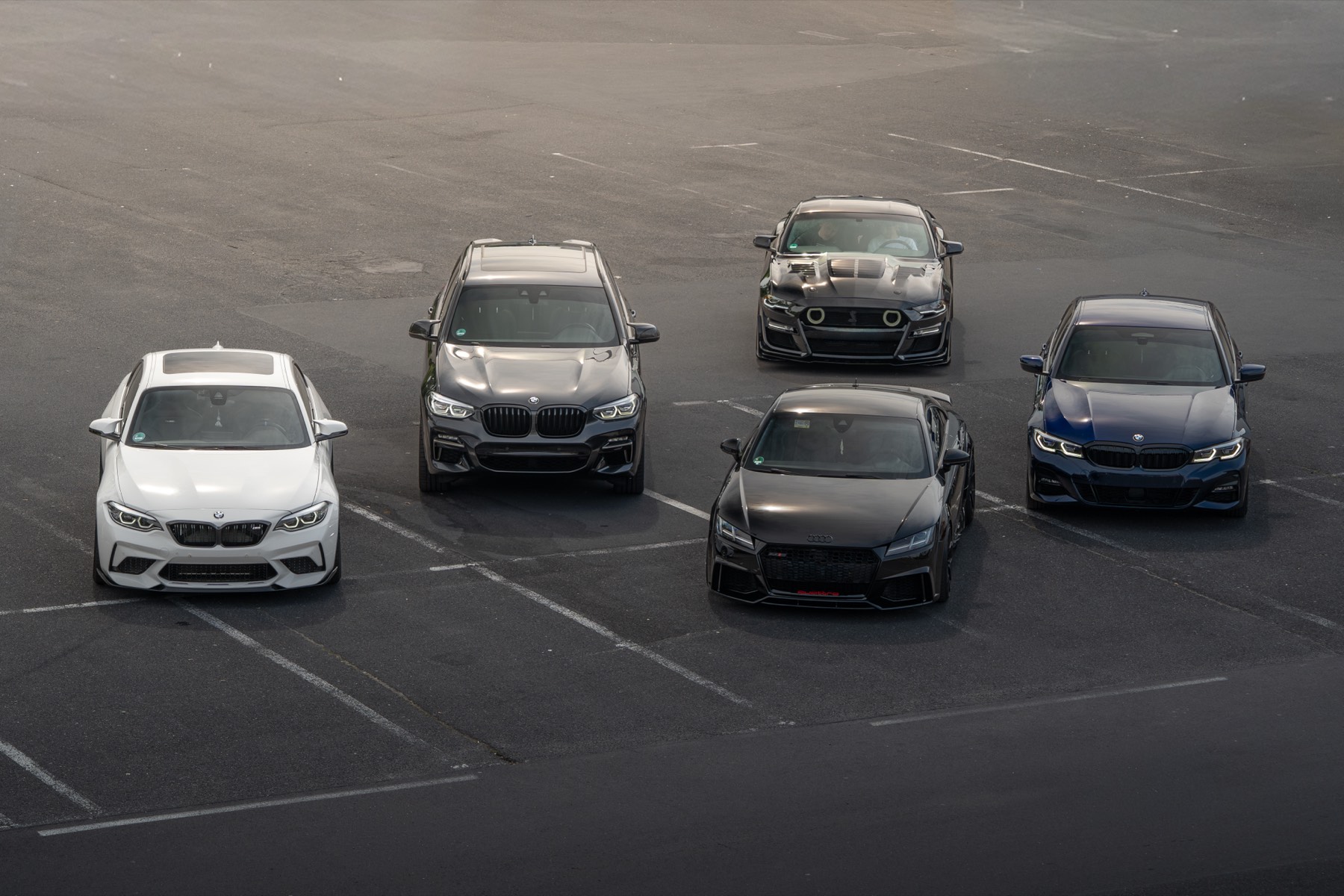 Fünf Fahrzeuge im Halbkreis auf einem leeren Parkplatz, von oben fotografiert