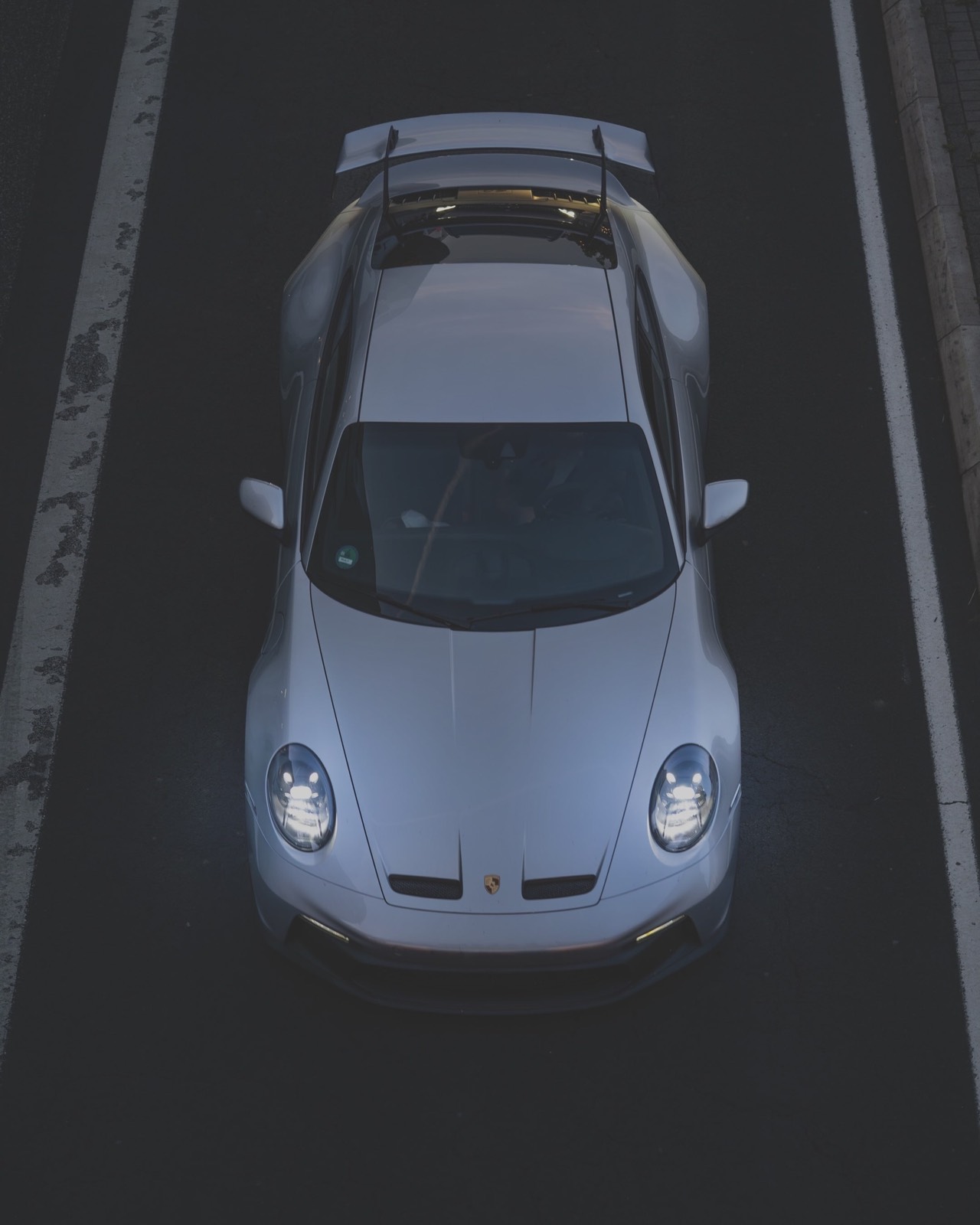 Silberner Porsche 911 GT3 von oben auf dunklem Asphalt